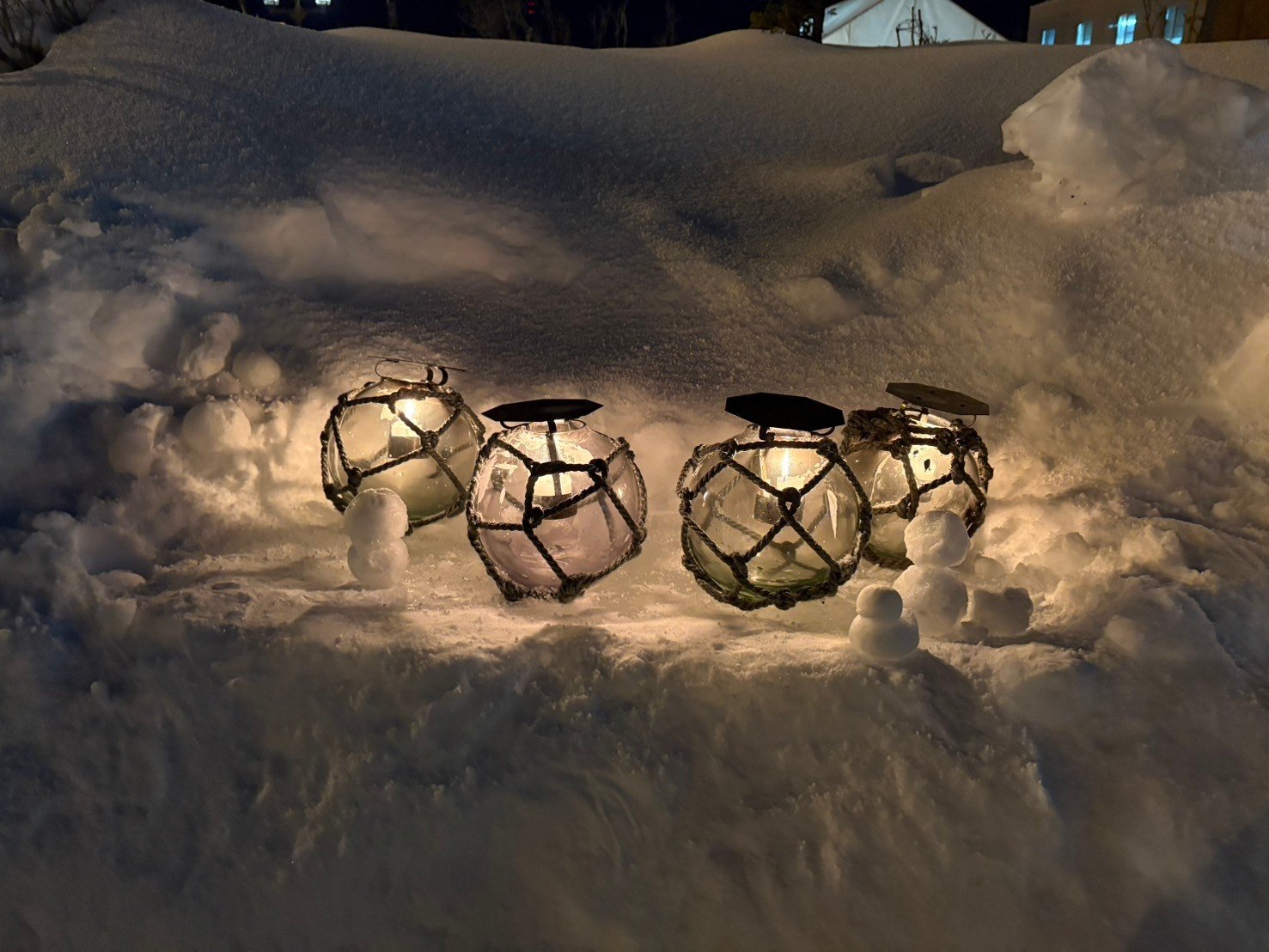 雪の上に並ぶ、網をかけたガラス浮き玉のキャンドルと小さな雪だるま。夜の小樽雪あかりの路