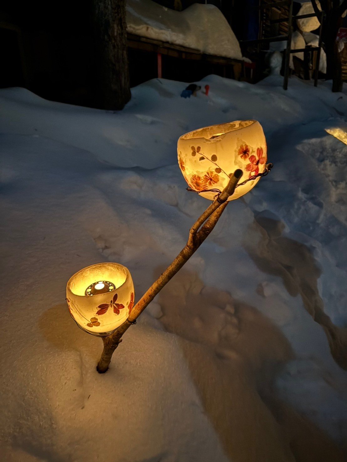 雪の中に立てた木の枝に灯る、押し花模様の丸い雪あかりの灯り二つ