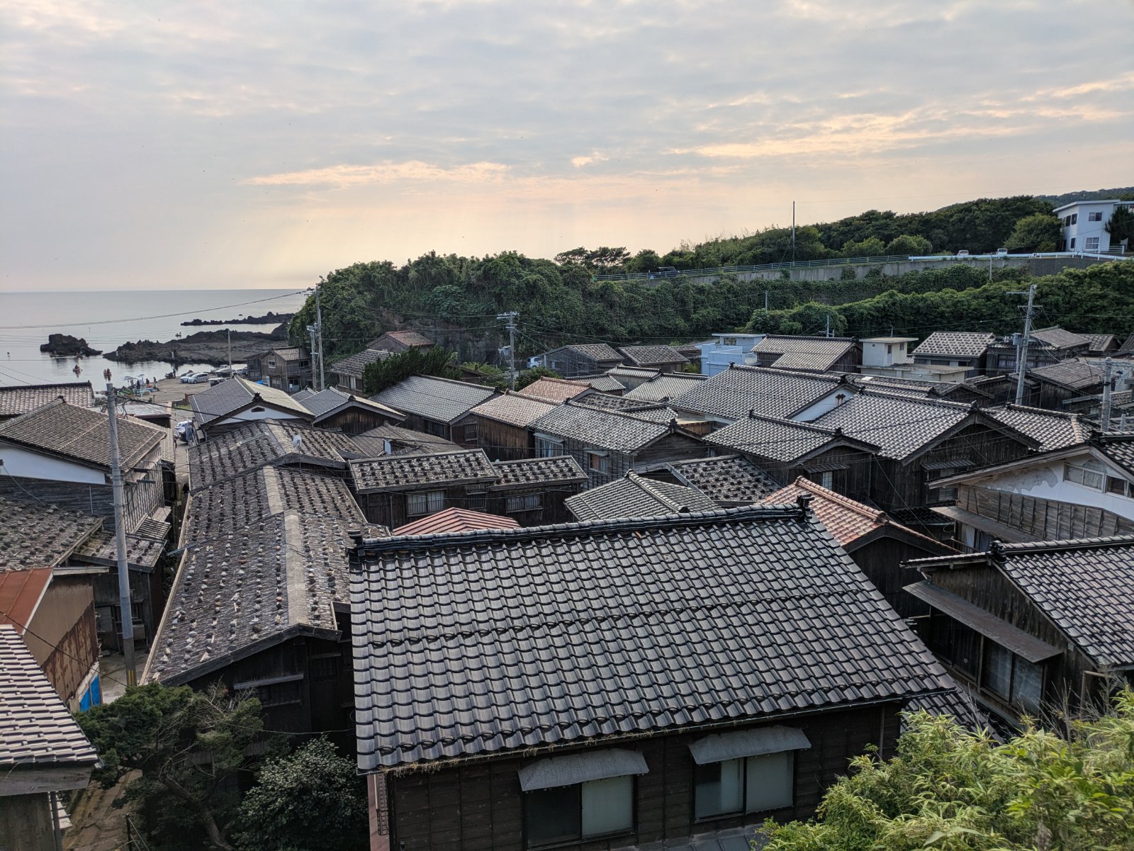 高台から見下ろす宿根木集落の瓦屋根の家並みと夕方の海