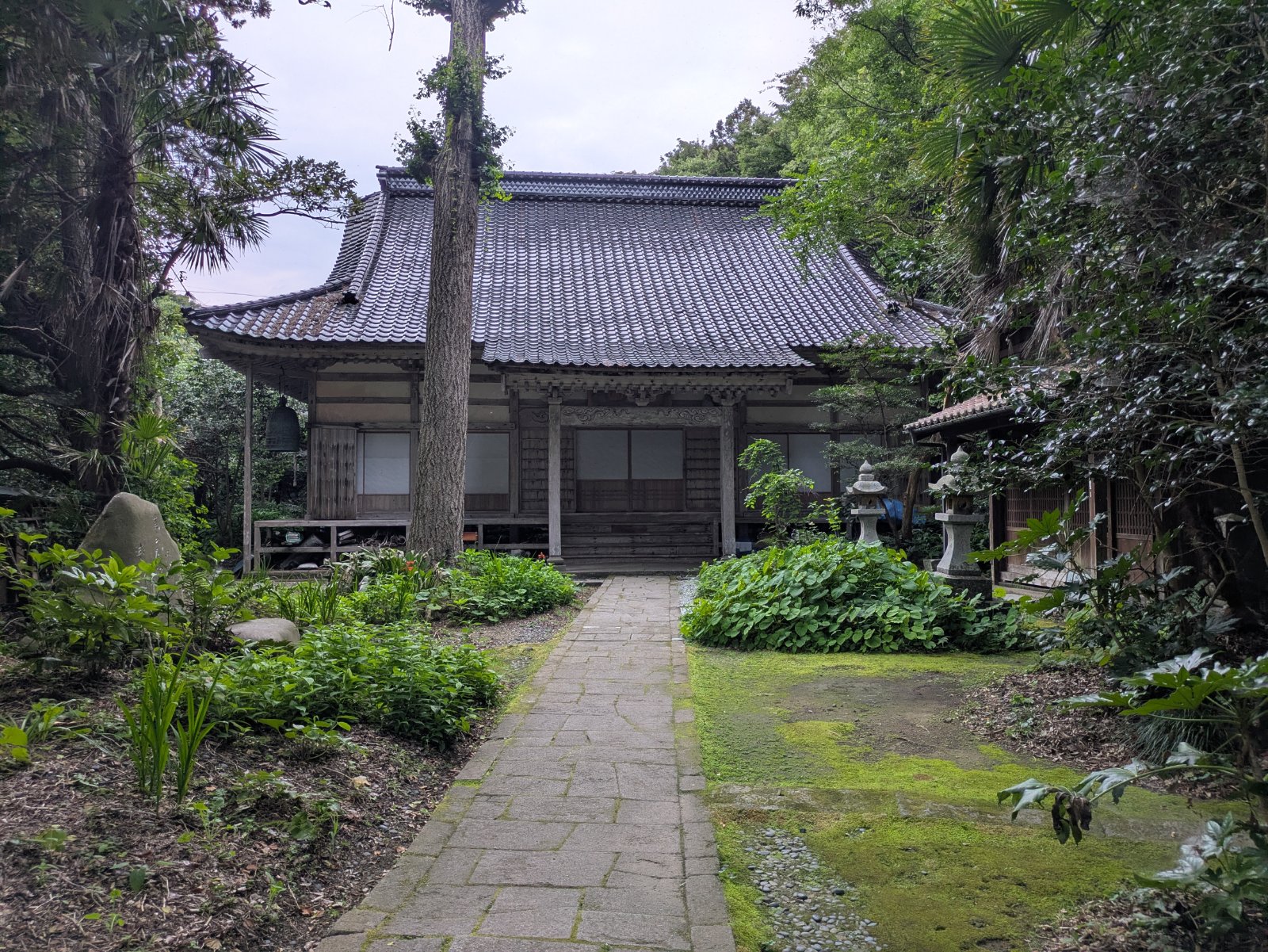 宿根木集落の奥にある寺の本堂。緑に囲まれた石畳の参道と苔むした庭、石灯籠