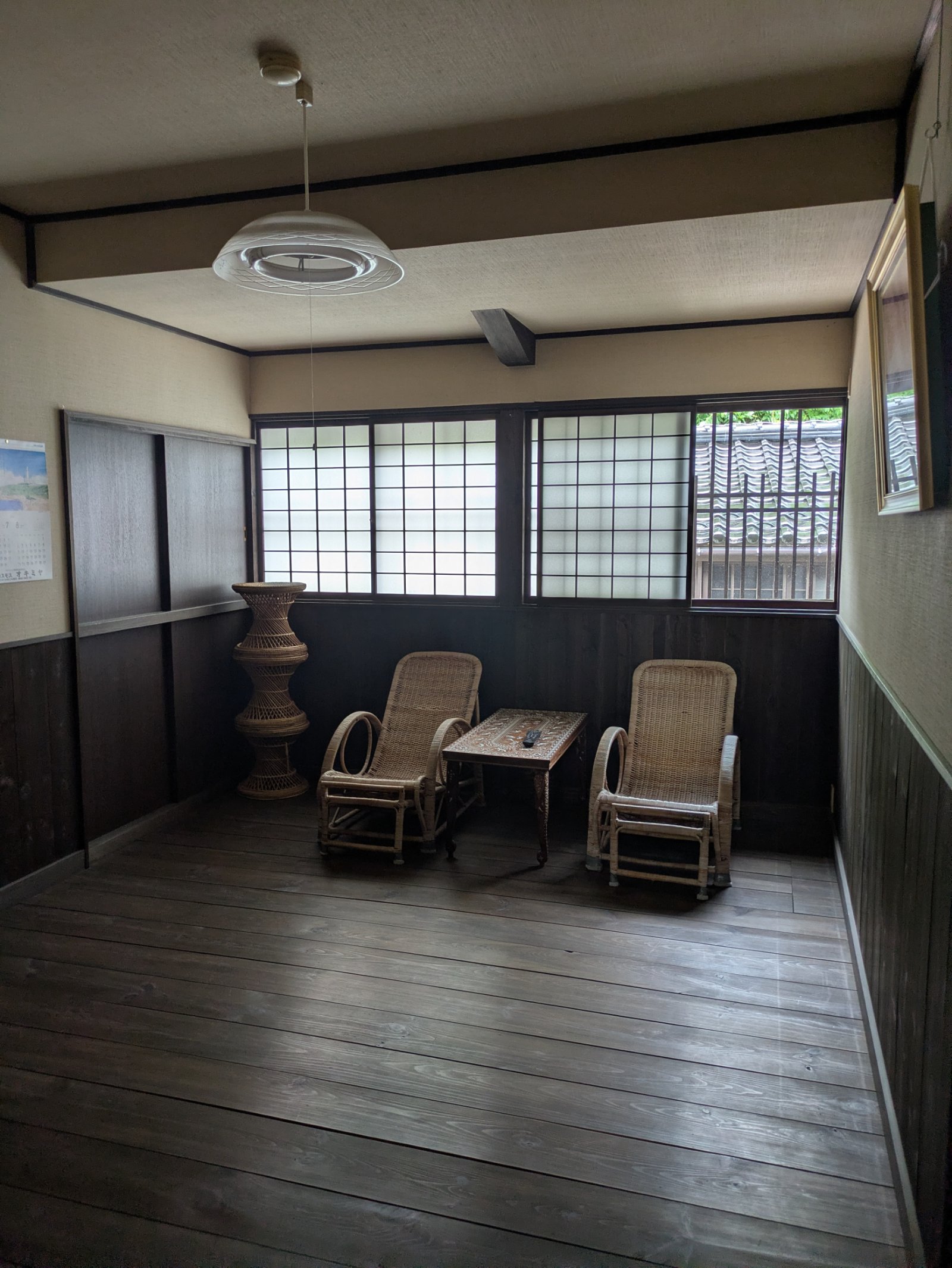 板張りの床の部屋に籐の椅子2脚と低いテーブル、格子窓の外に瓦屋根