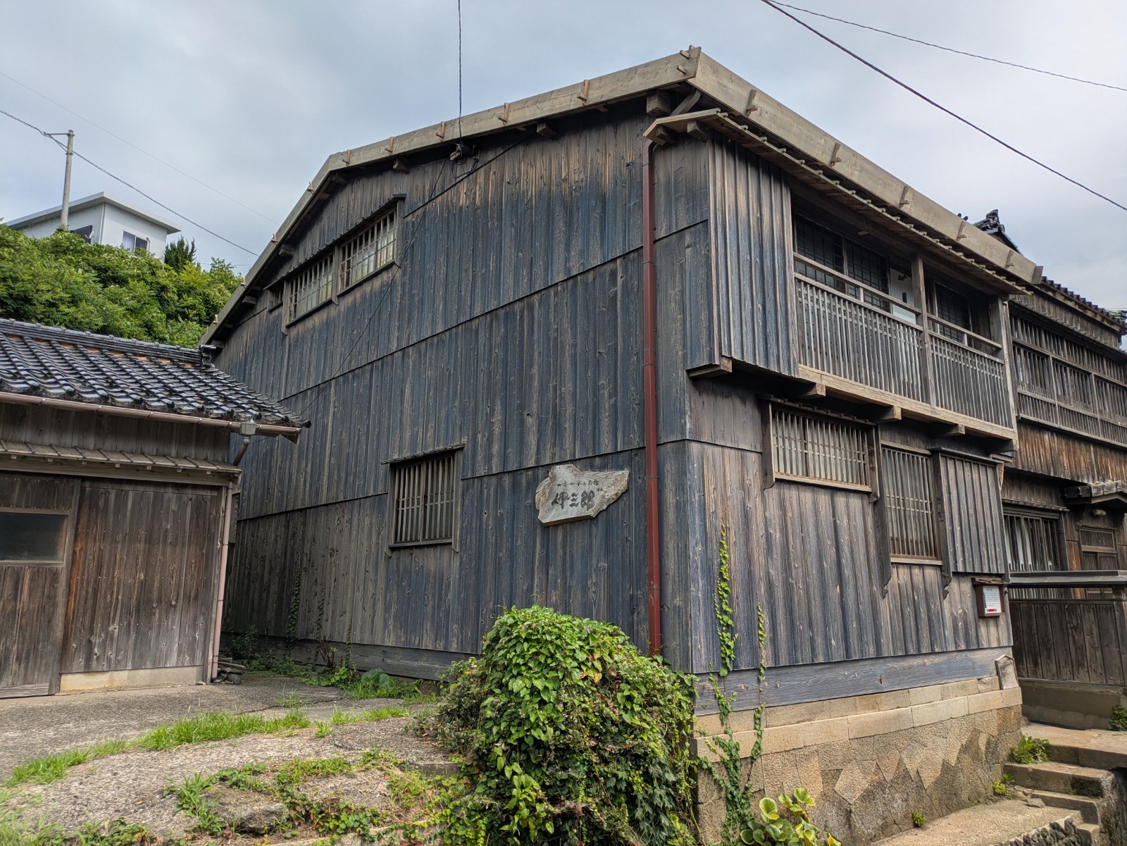 宿根木集落に建つ一棟貸しの宿「伊三郎」の外観。板張りの木造二階建てに石の表札が掛かる