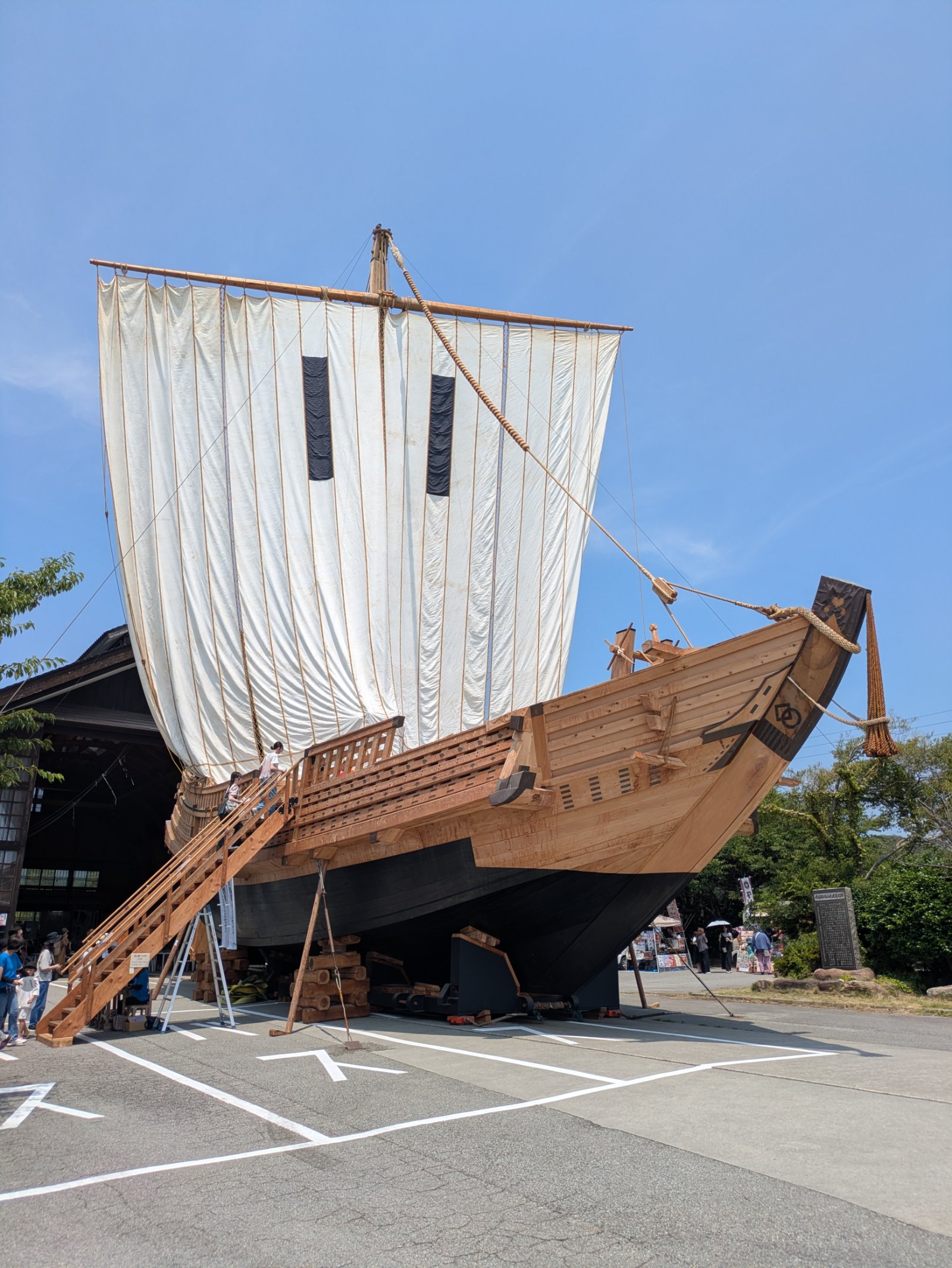 屋外に展示された北前船の復元船。白い帆を張った木造船に階段で上る見学者と夏の青空