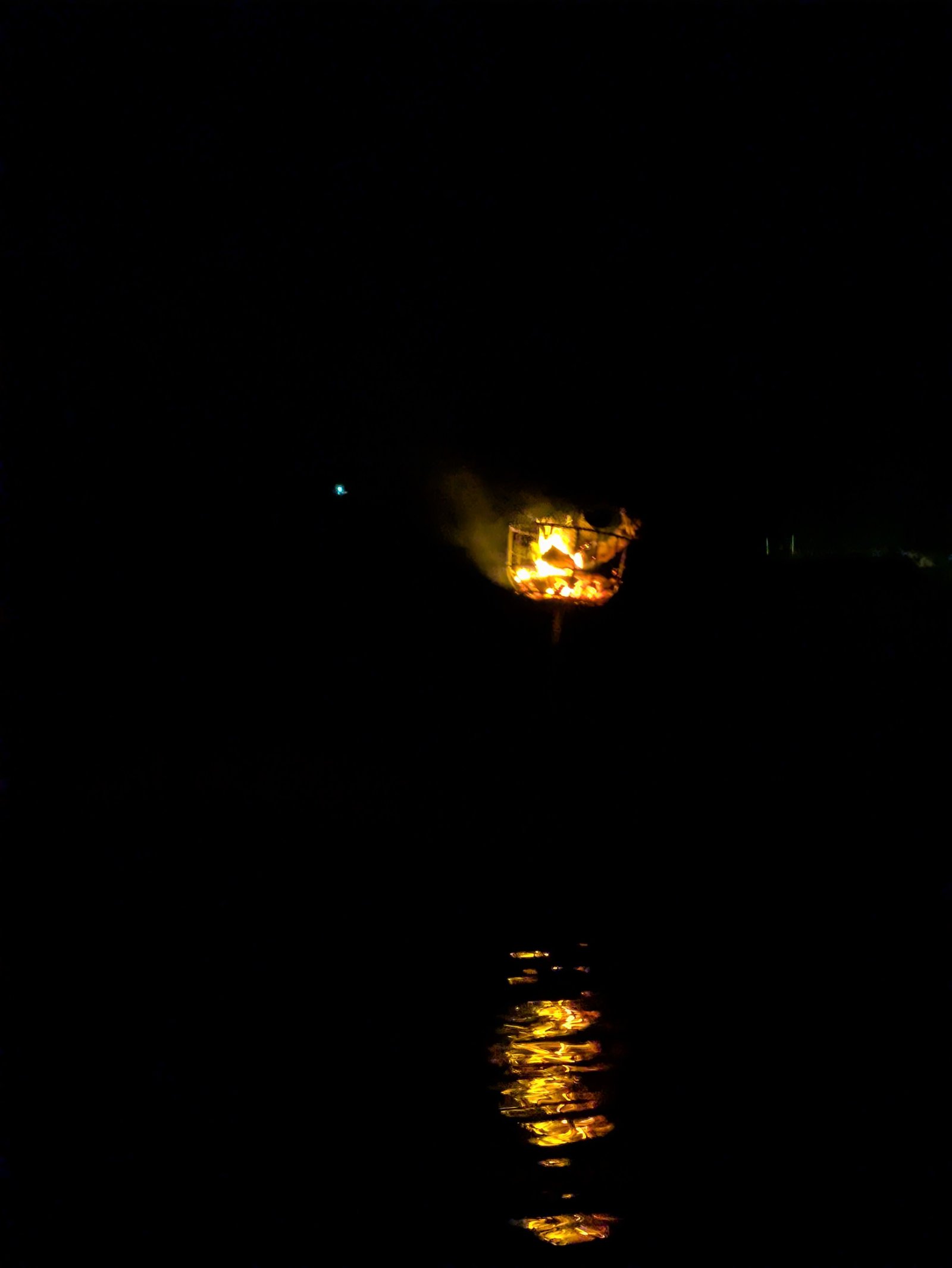 夜の暗闇に燃える岸辺のかがり火と水面に映る炎