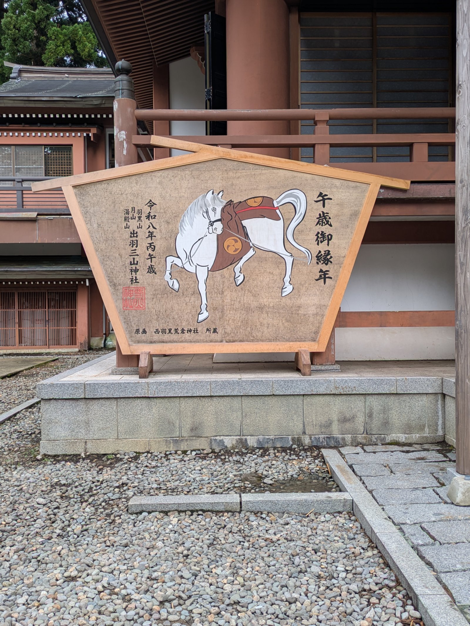 出羽三山神社の社殿前に立つ、白馬が描かれた「午歳御縁年」の大絵馬