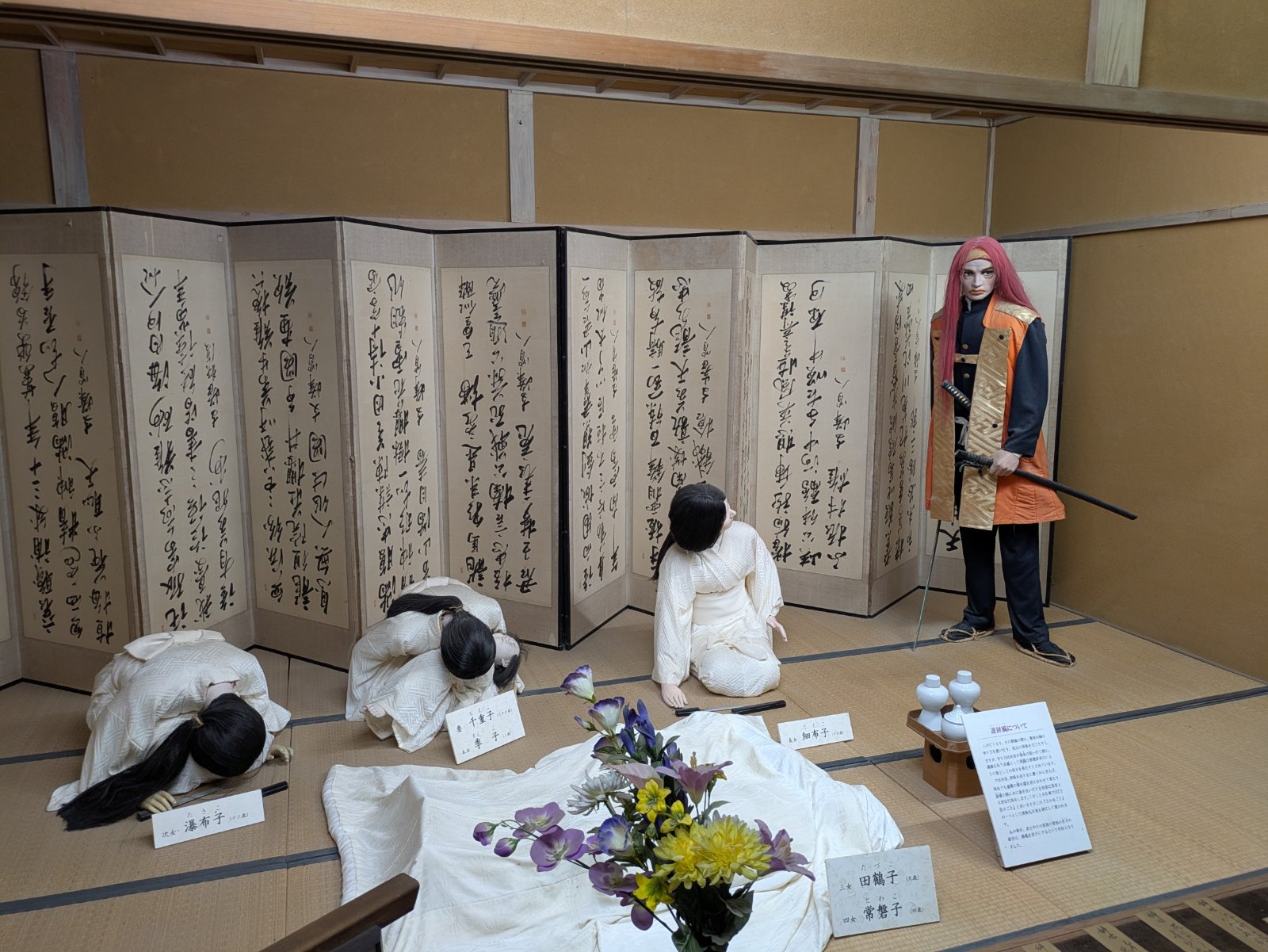 会津武家屋敷の自刃の部屋を再現した展示、白装束の女性たちの人形と書の屏風、刀を持つ赤い髪の武士の人形