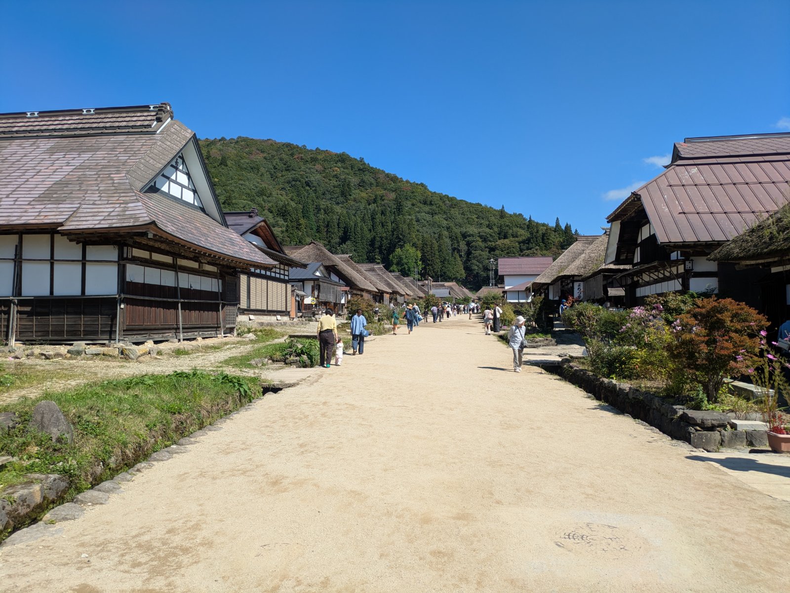 晴天の下、茅葺き屋根の家並みが続く大内宿の通りと散策する人々