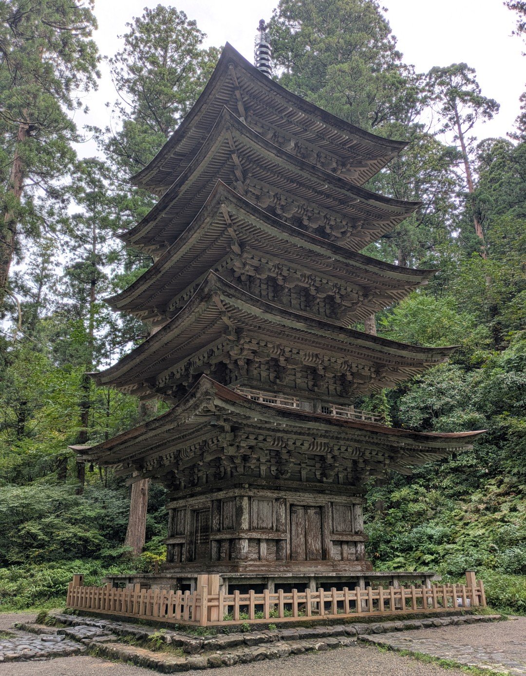 杉木立の中に立つ羽黒山の五重塔、木の柵に囲まれた曇りの日の境内