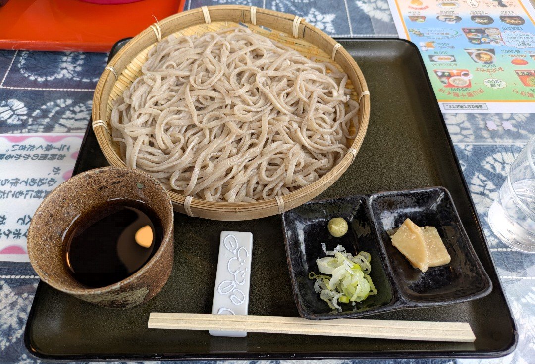 竹ざるに盛られた十割蕎麦と、そばつゆ、ねぎ、わさび、漬物が並ぶ盆