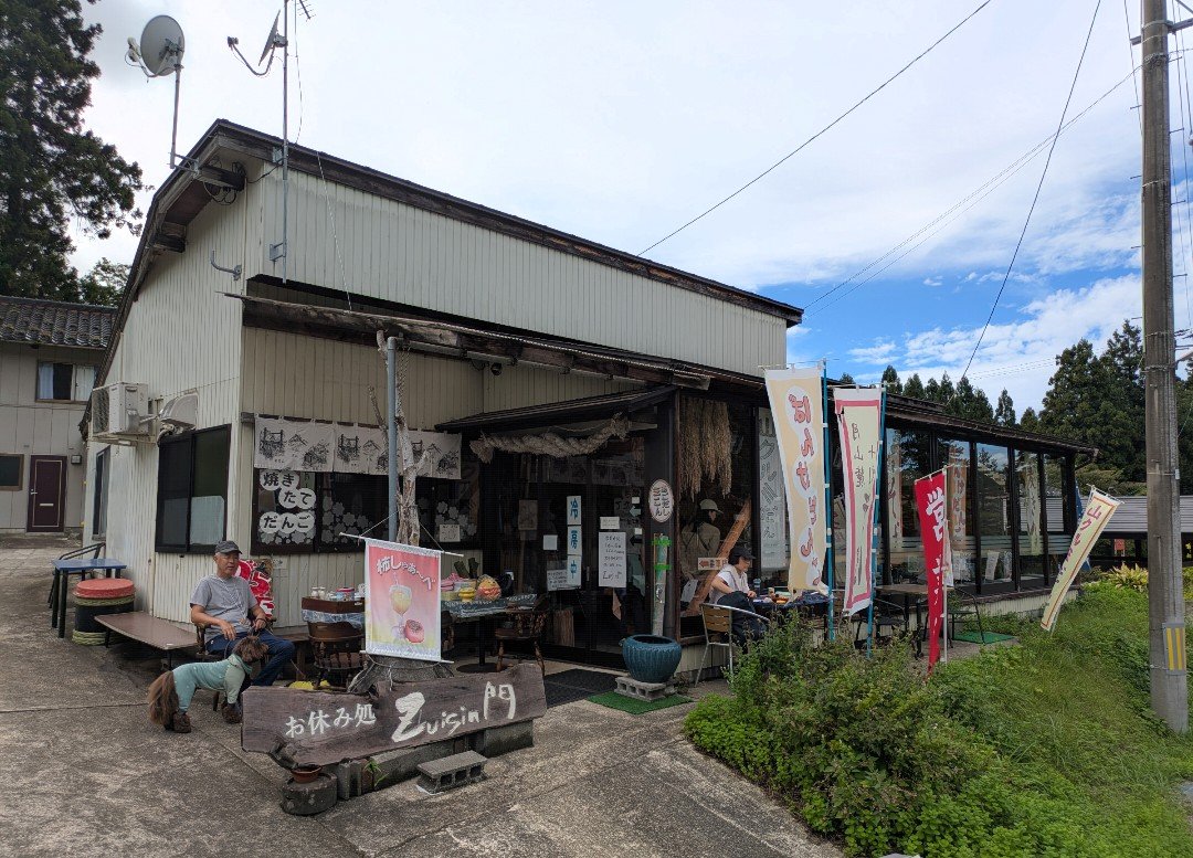 羽黒山の門前にある「お休み処Zuisin門」の外観。のぼり旗が並び、店先で犬を連れた男性が休んでいる