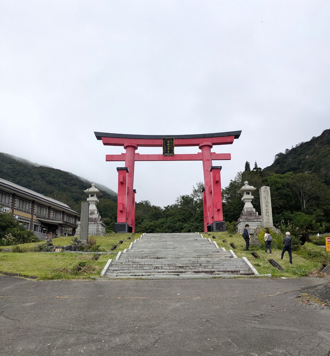曇り空の下、石段の上に立つ湯殿山の朱色の大鳥居と石灯籠