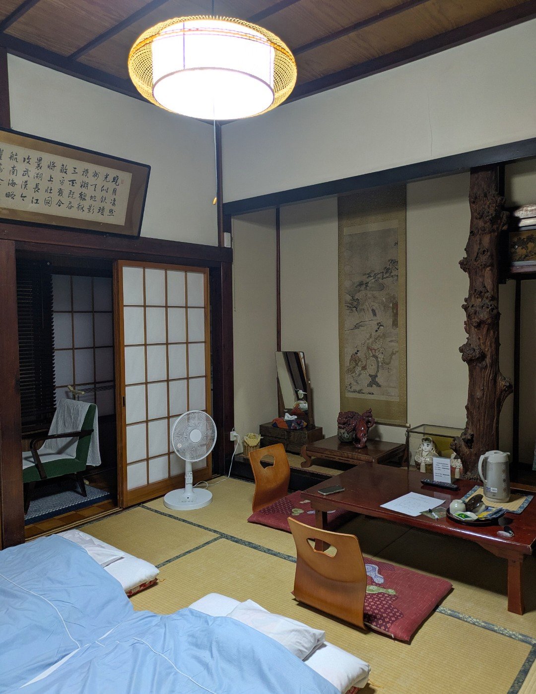 多聞館の和室。畳に布団が敷かれ、座卓と座椅子、床の間に掛け軸と自然木の床柱がある