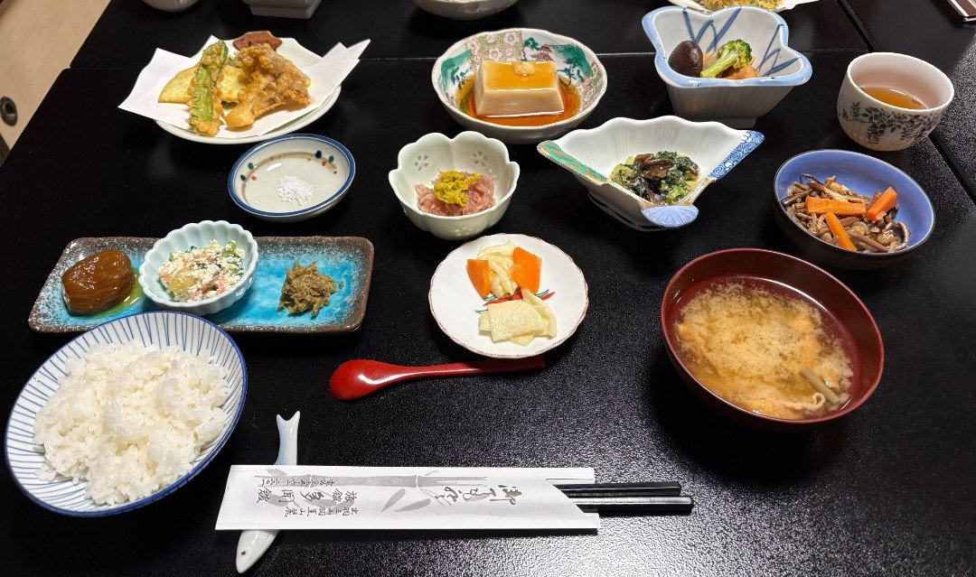 宿坊・多聞館の精進料理の夕食。ご飯、味噌汁、天ぷら、ごま豆腐などの小鉢が黒い卓に並ぶ