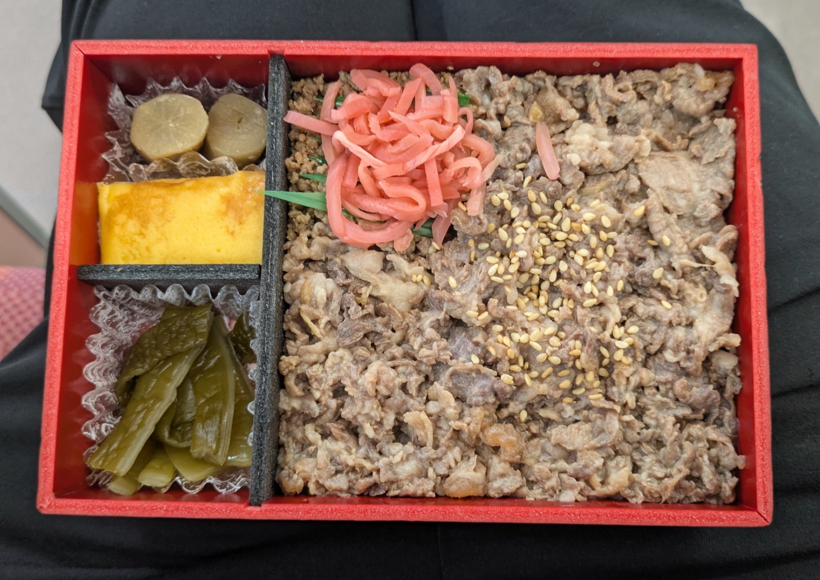 赤い折箱に詰められた牛肉の駅弁、紅しょうがや卵焼き、漬物入り