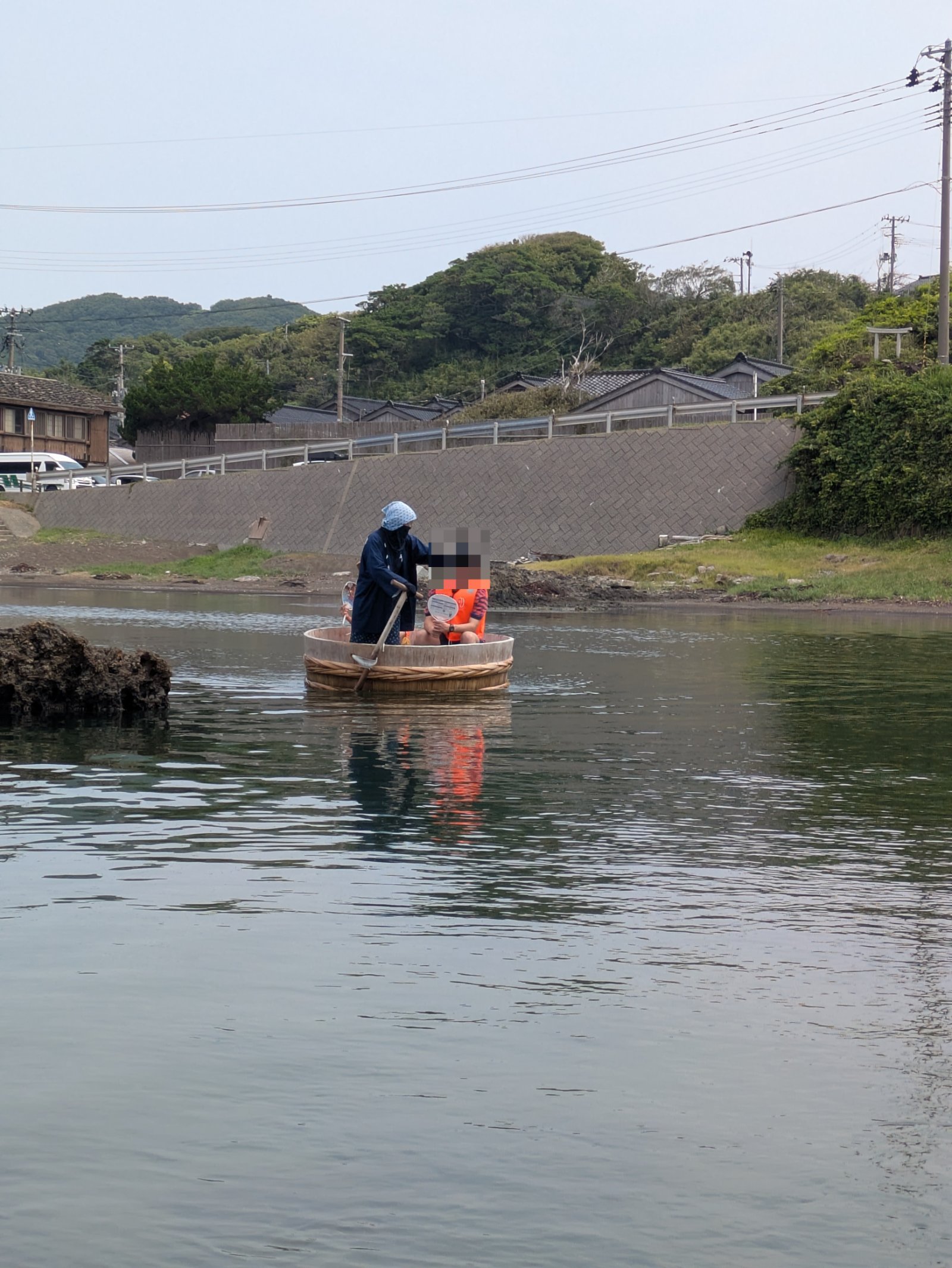 宿根木の入り江で、頭巾姿の船頭が一本の櫂でこぐたらい船に乗る救命胴衣姿の乗客