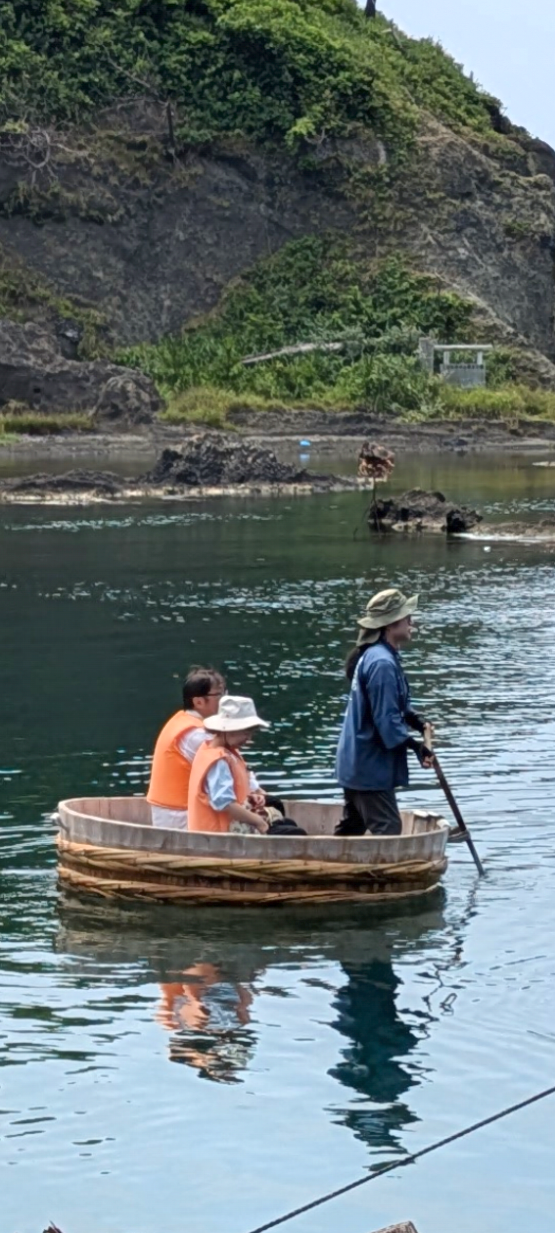 佐渡島の宿根木の入り江で、一本の櫂を操る船頭とライフジャケット姿の乗客2人を乗せたたらい船