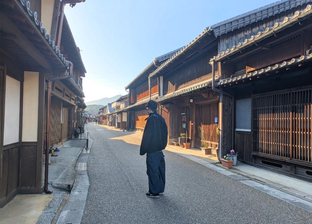 朝の光が差す関宿の通りに立つ人と、両側に並ぶ格子戸の木造町家