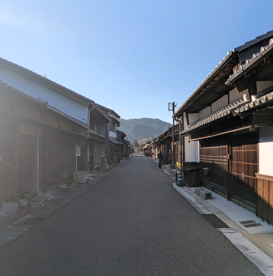 晴れた日の関宿、木造の町家が両側に並ぶ旧東海道の一本道と奥の山並み
