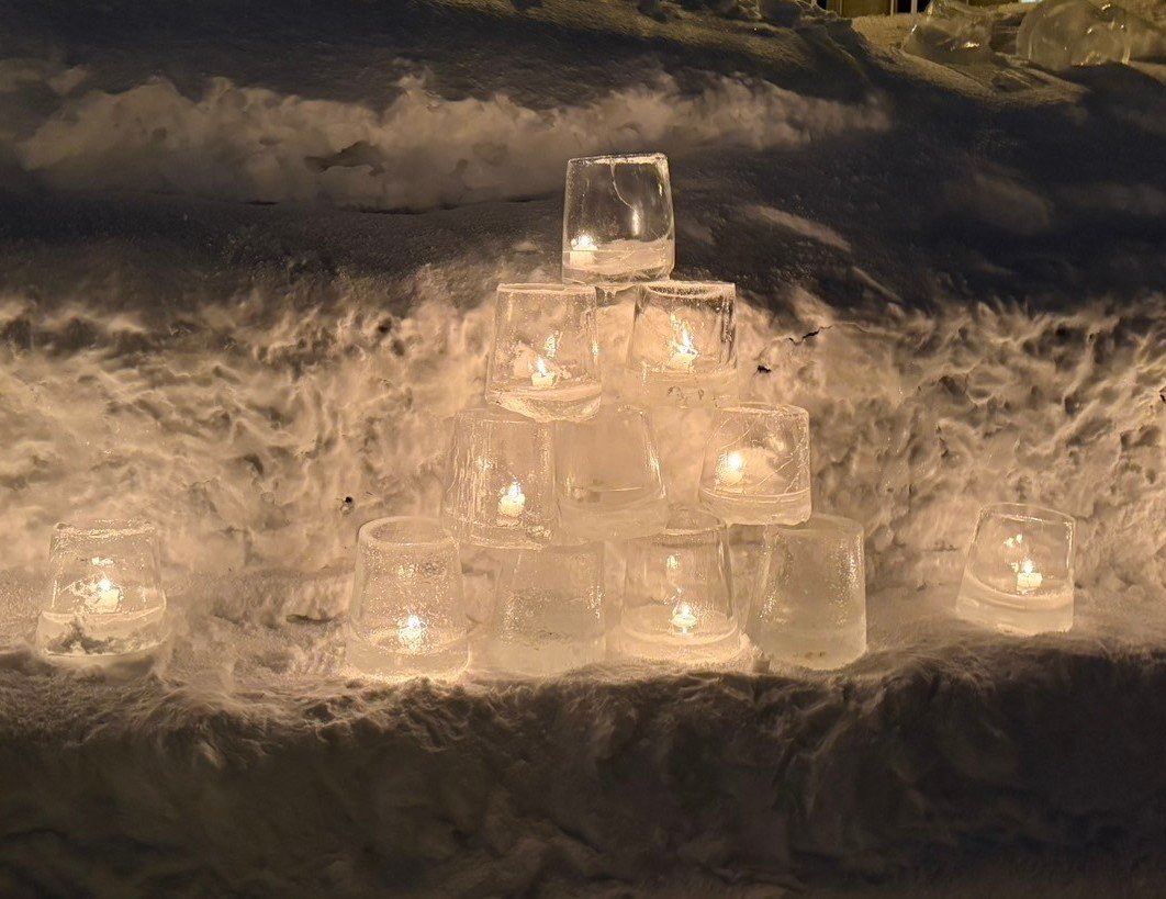 雪の斜面にピラミッド状に積まれた、ろうそくが灯る氷のキャンドル(夜)