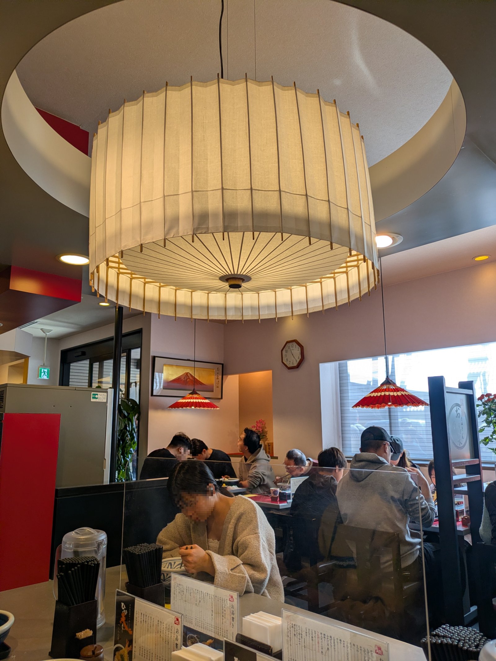和傘形の大きな照明が下がるおか泉の店内、テーブル席でうどんを食べる客たち