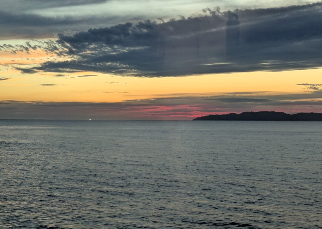 新潟と山形の県境付近の海に沈む夕焼け、厚い雲の下に赤く染まる空と島影