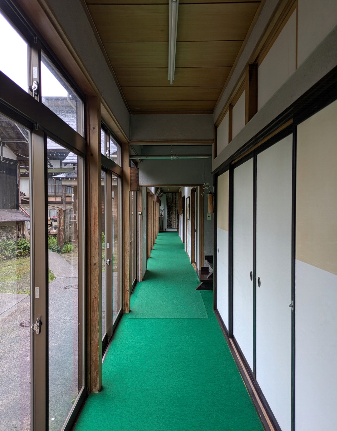 大進坊の館内の廊下。緑のカーペットが敷かれ、片側にガラス戸、反対側に襖が並ぶ